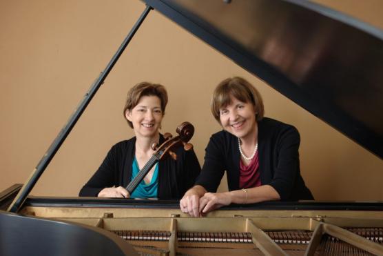 A photo of cellist Susan Lamb Cook holder a cello and pianist Gayle Blankenburg sitting at a piano.