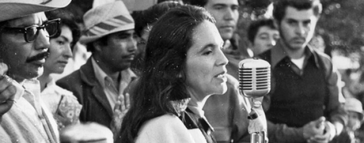 Dolores Huerta speaking into a microphone at a rally.
