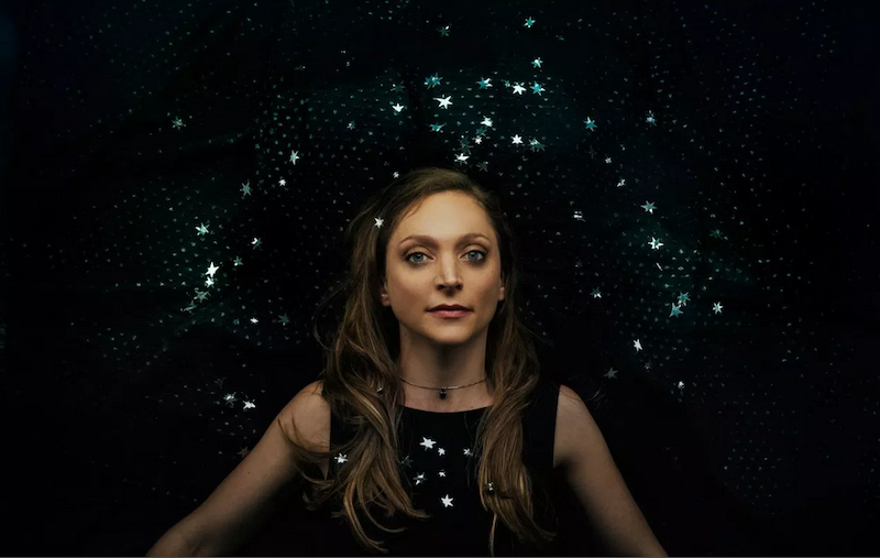 A portrait of Eilen Jewell in front of a black background with diamons-like jewels on it.