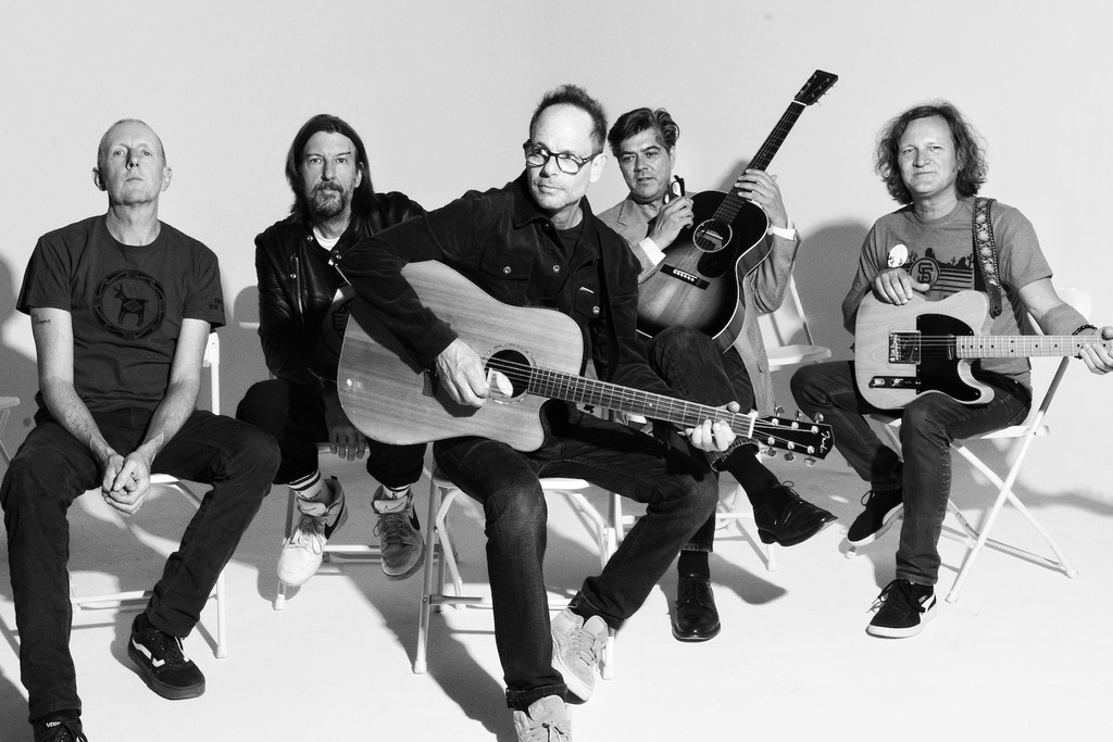 A back-and-white photo of the band sitting in front of a white backkground.