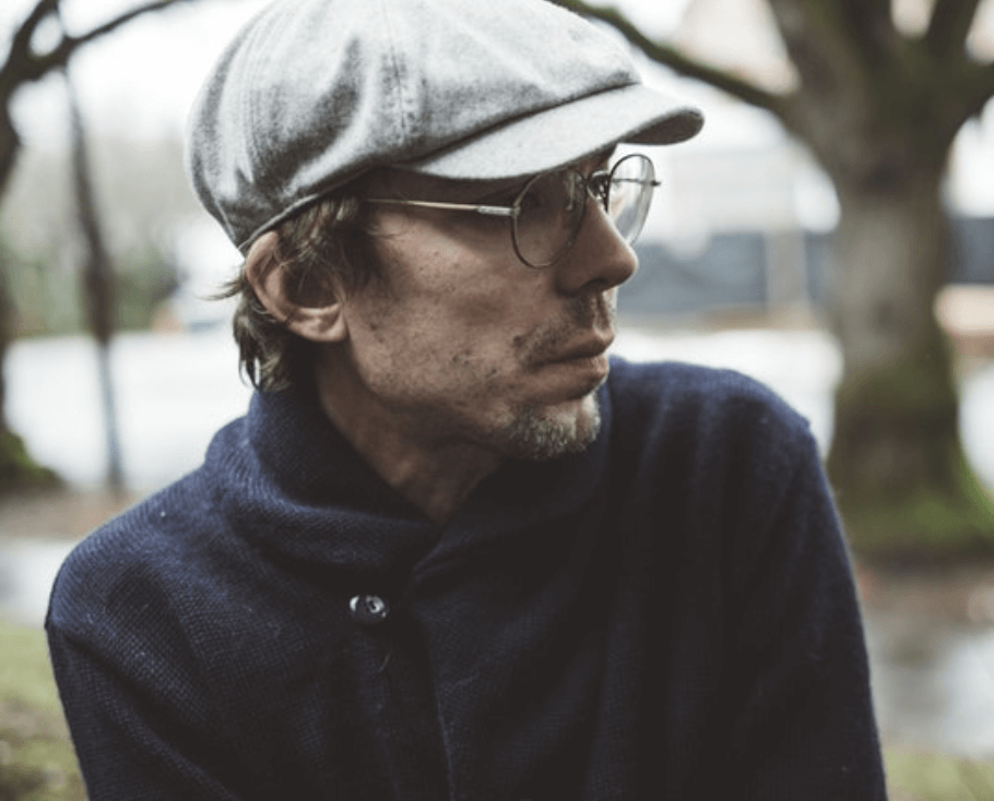 Justin Townes Earle wearing a cap and round-rimmed glasses.