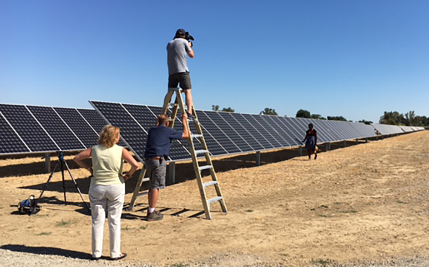 A cameraman stands on a ladder at a solar farm