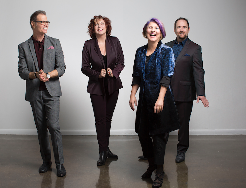 The four members of the Manhattan Transfer standing, smiling and laughing.