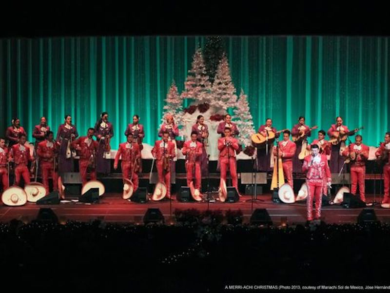 Mariachi Sol de Mexico performing on stage with Christmas trees in the baackground.