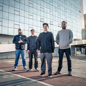 A photo of the band standing in front of a modern glass-sheathed building.
