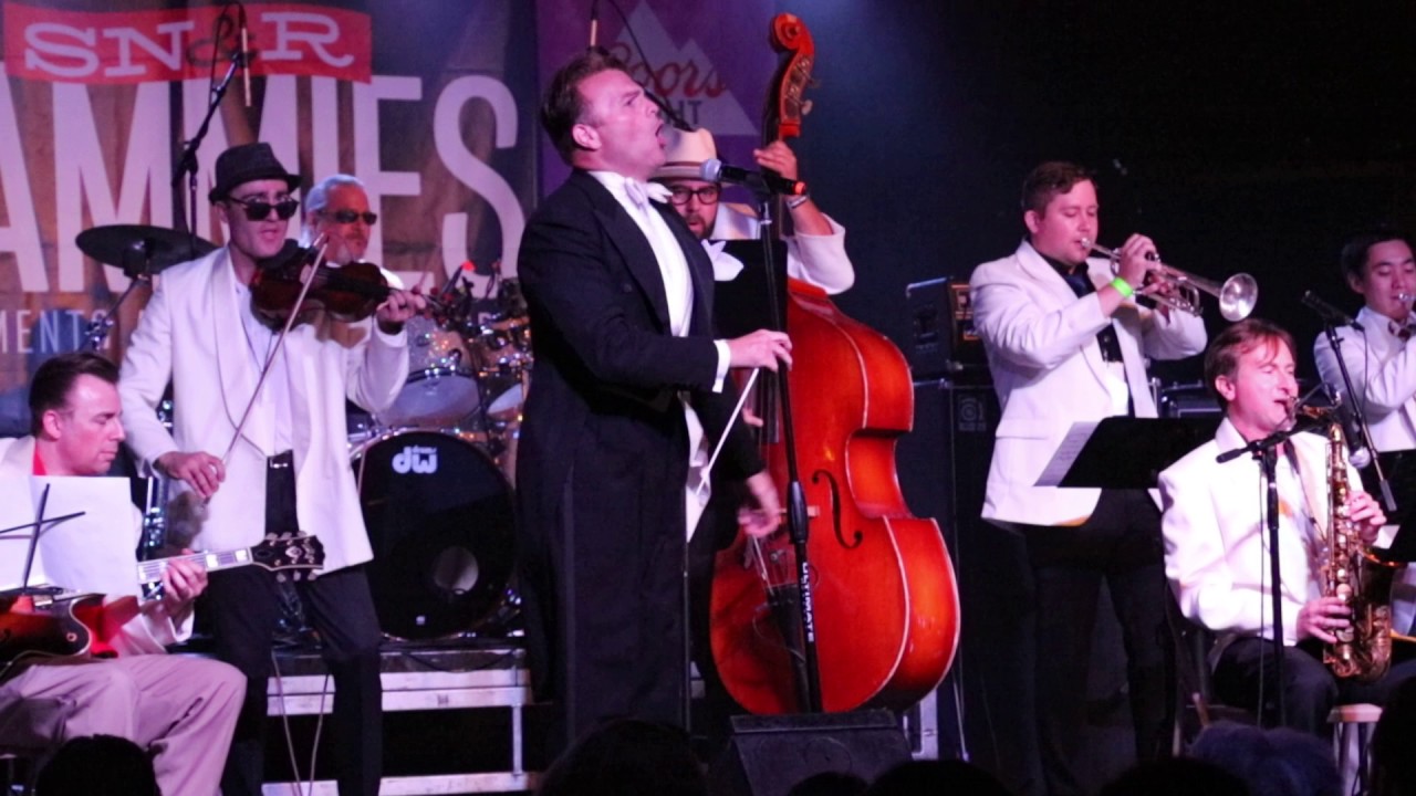 Peter Petty singing on stage while wearing a tuxedo and fronting a big band.