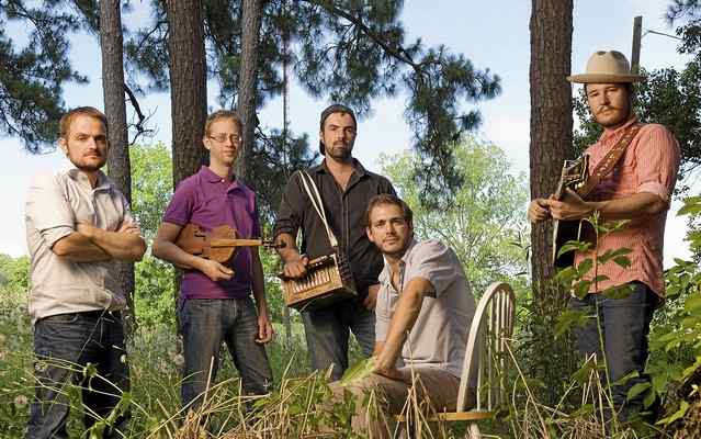 A photo of members of the band holding musical instruments and stading among trees.