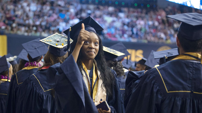 A female graduate gives a thumbs up at commencement